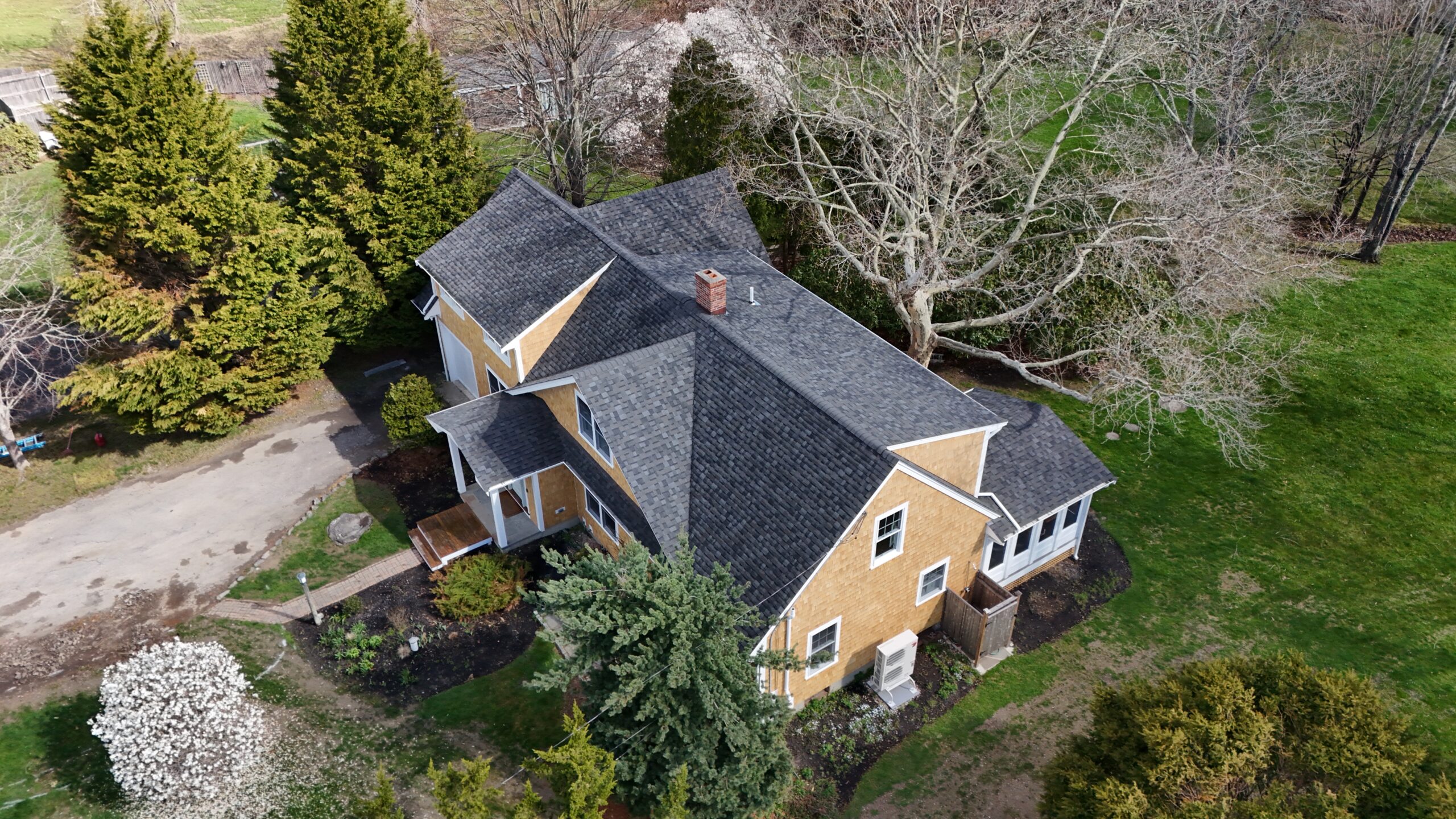 Aerial view of a yellow house with a dark gray shingled roof surrounded by trees and green lawn.